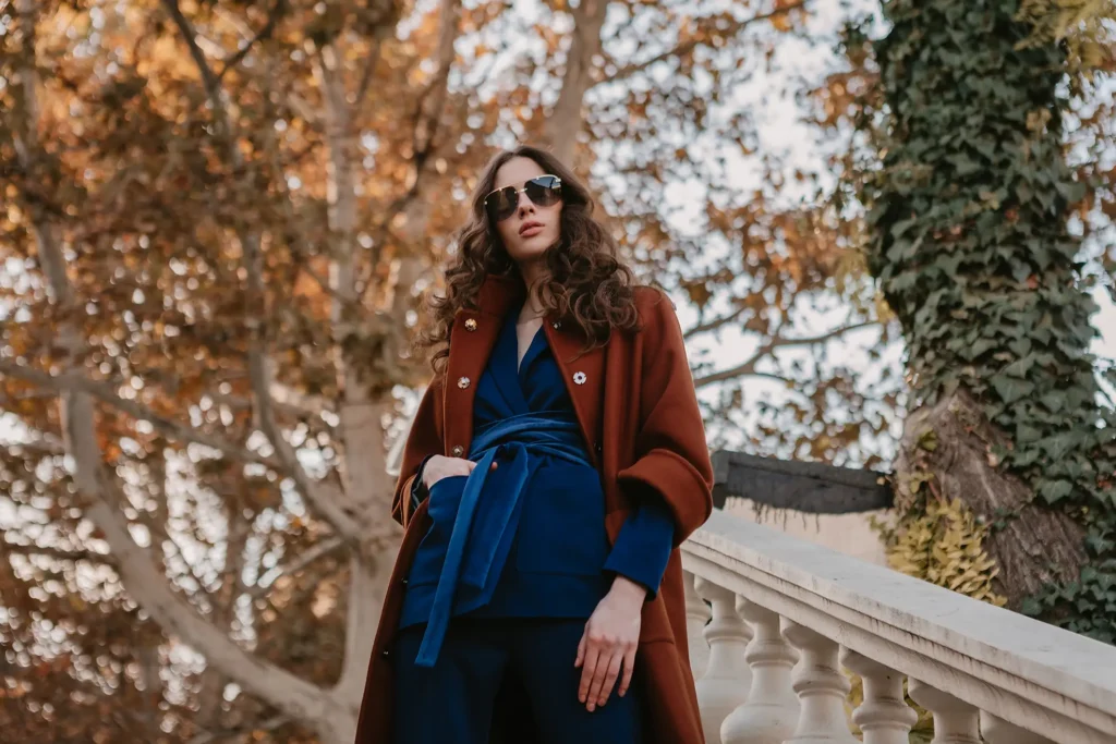 belle elegante femme maigre souriante aux cheveux boucles marchant dans les escaliers de la rue vetue d un manteau brun chaud et d un costume bleu style de rue a la mode automne 1
